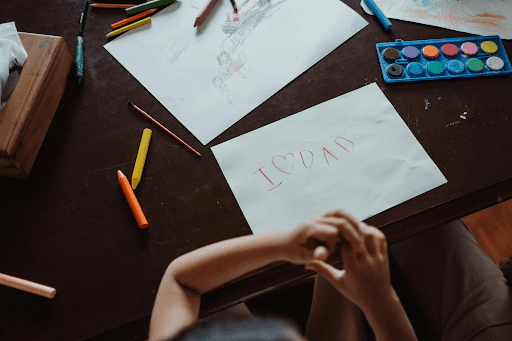 Child sitting at a table with colorful crayons, drawings, and a handwritten note